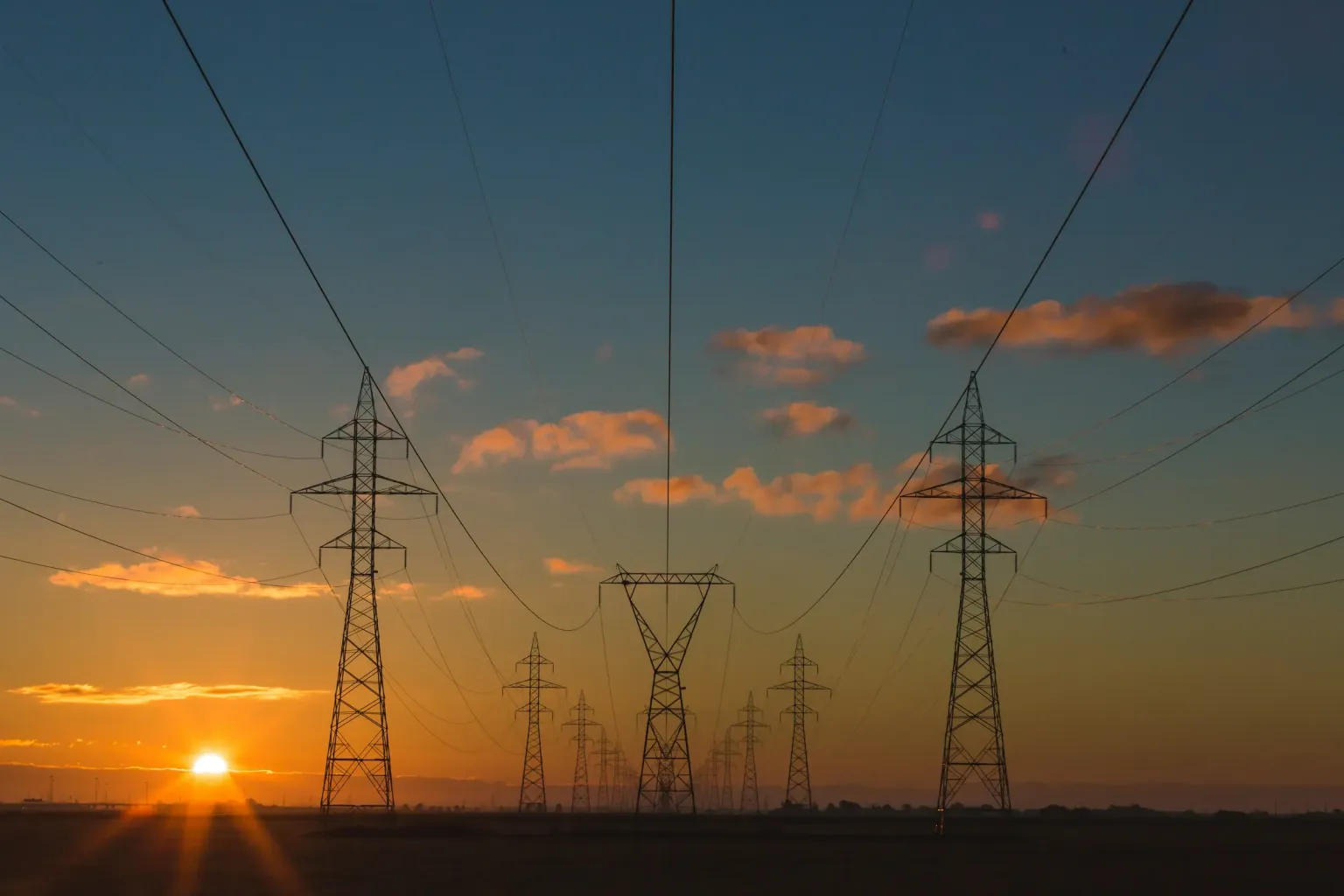 Hochspannungsmasten und Stromleitungen vor einem Abendhimmel mit tief stehender Sonne